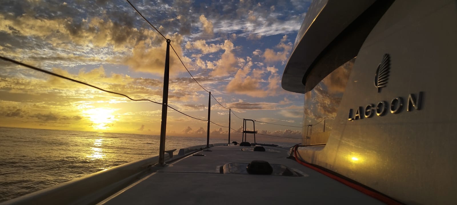 Lagoon 42 2021 Passavant Coucher de soleil sur l'eau avec un bateau à voile en premier plan.