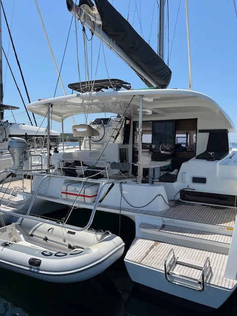 Lagoon 42 2021 Vue arrière Catamaran blanc amarré au port, avec un petit bateau à moteur à côté.