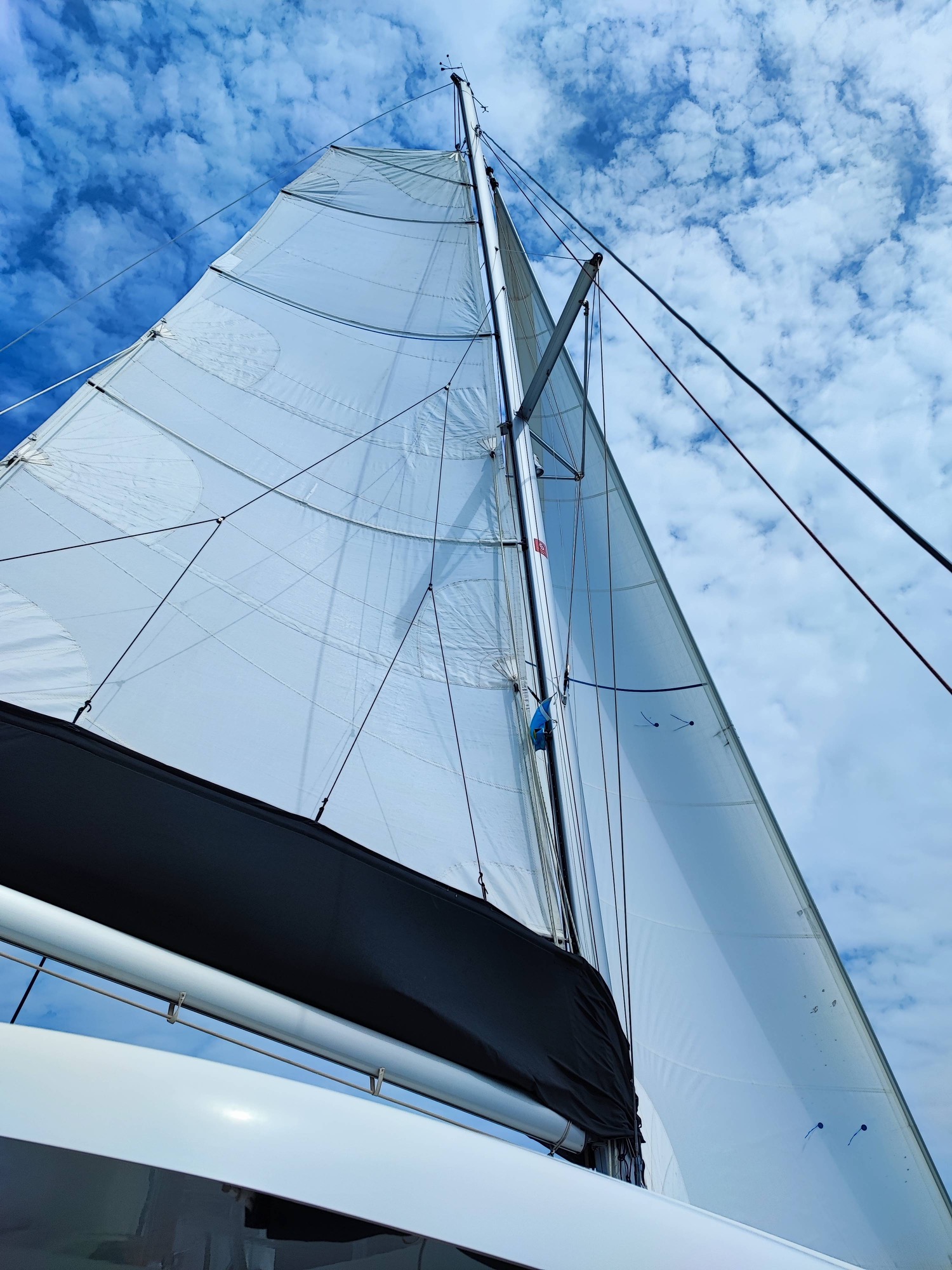 Lagoon 42 2021 Sous voiles Grand mât de voilier avec voiles blanches, ciel bleu en arrière-plan.