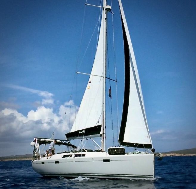 Voilier blanc amarré dans un port, avec des mâts et un ciel nuageux en arrière-plan.