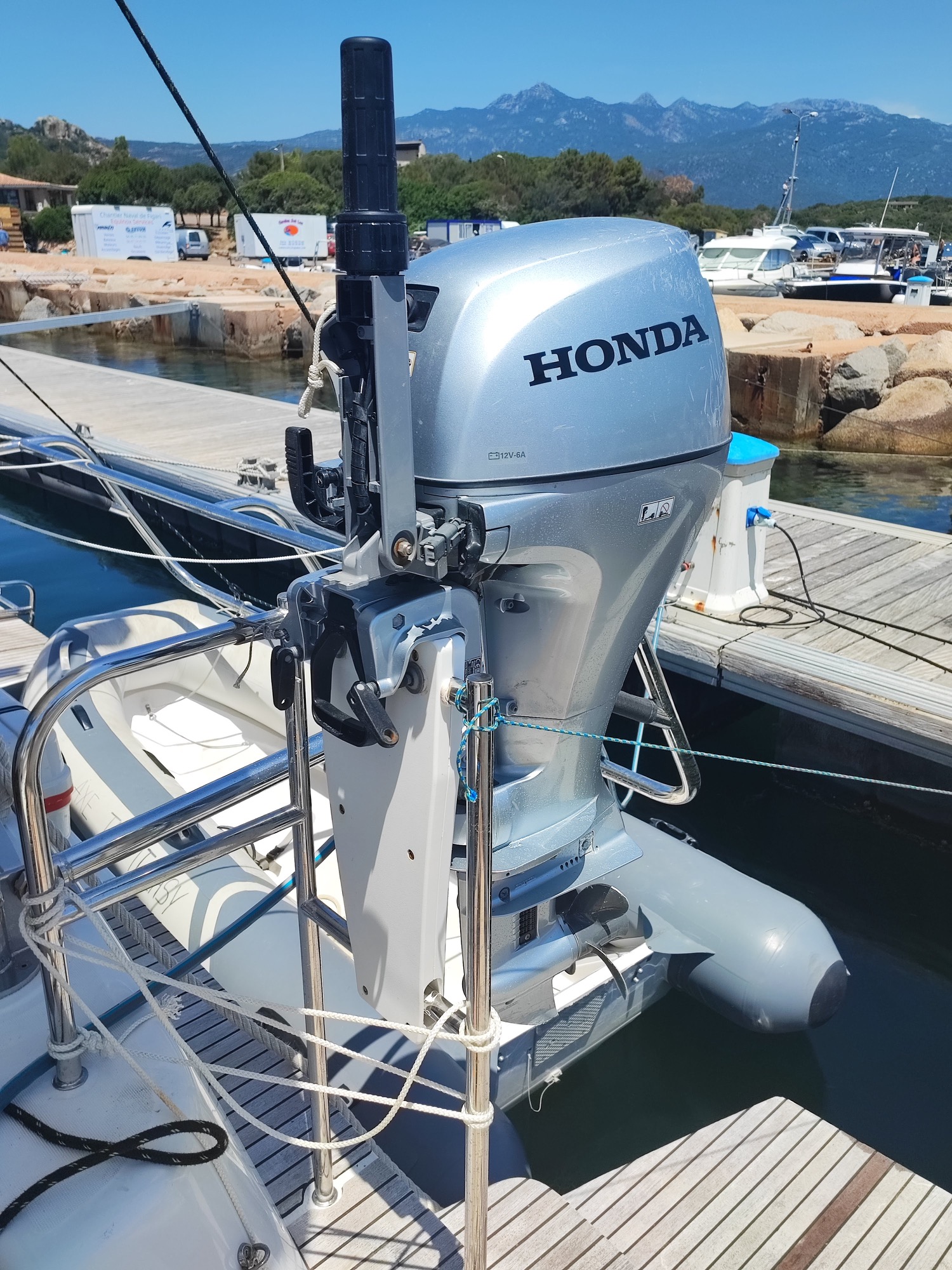 Lagoon 42 2021 Moteur annexe Honda 10 cv Moteur hors-bord Honda monté sur un bateau au port, avec des montagnes en arrière-plan.
