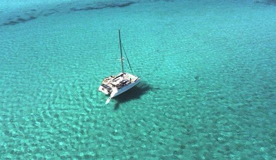 Voilier blanc accosté dans un port, avec d'autres bateaux en arrière-plan. Ciel nuageux.