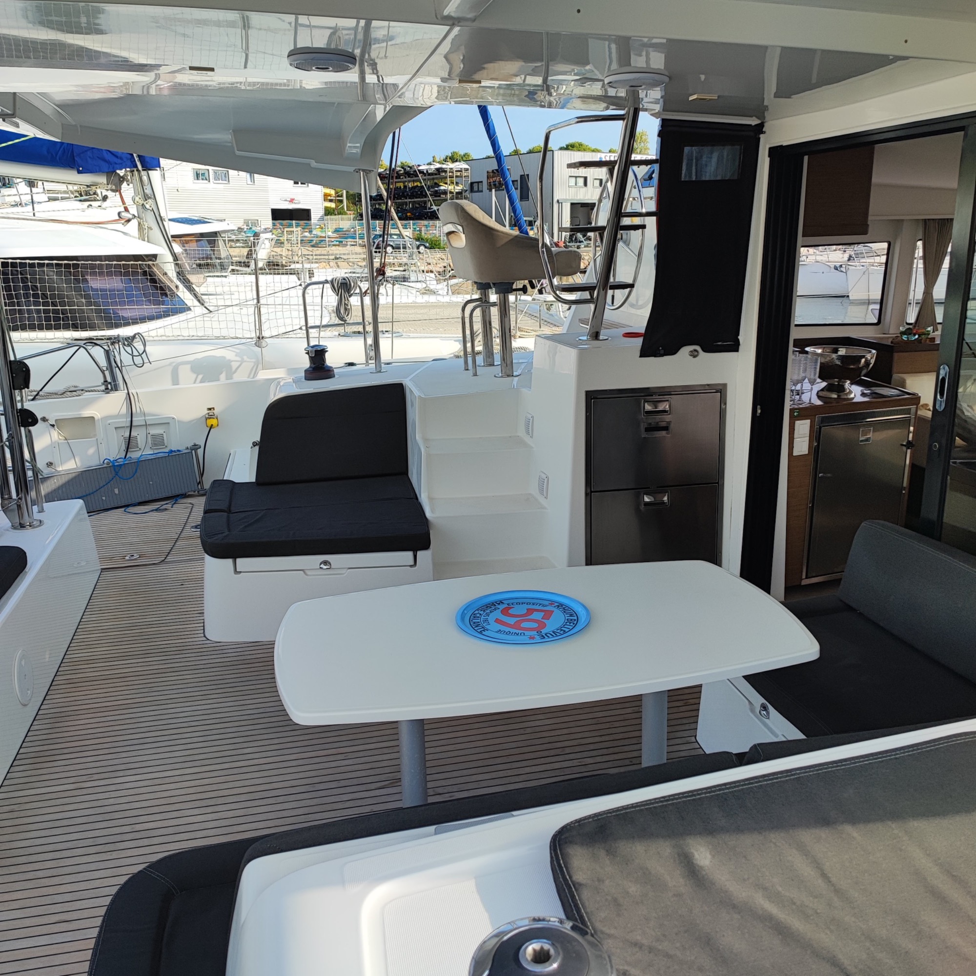 Lagoon 42 2021 Cockpit Terrasse d'un bateau avec des sièges et une table, vue sur un port de plaisance.