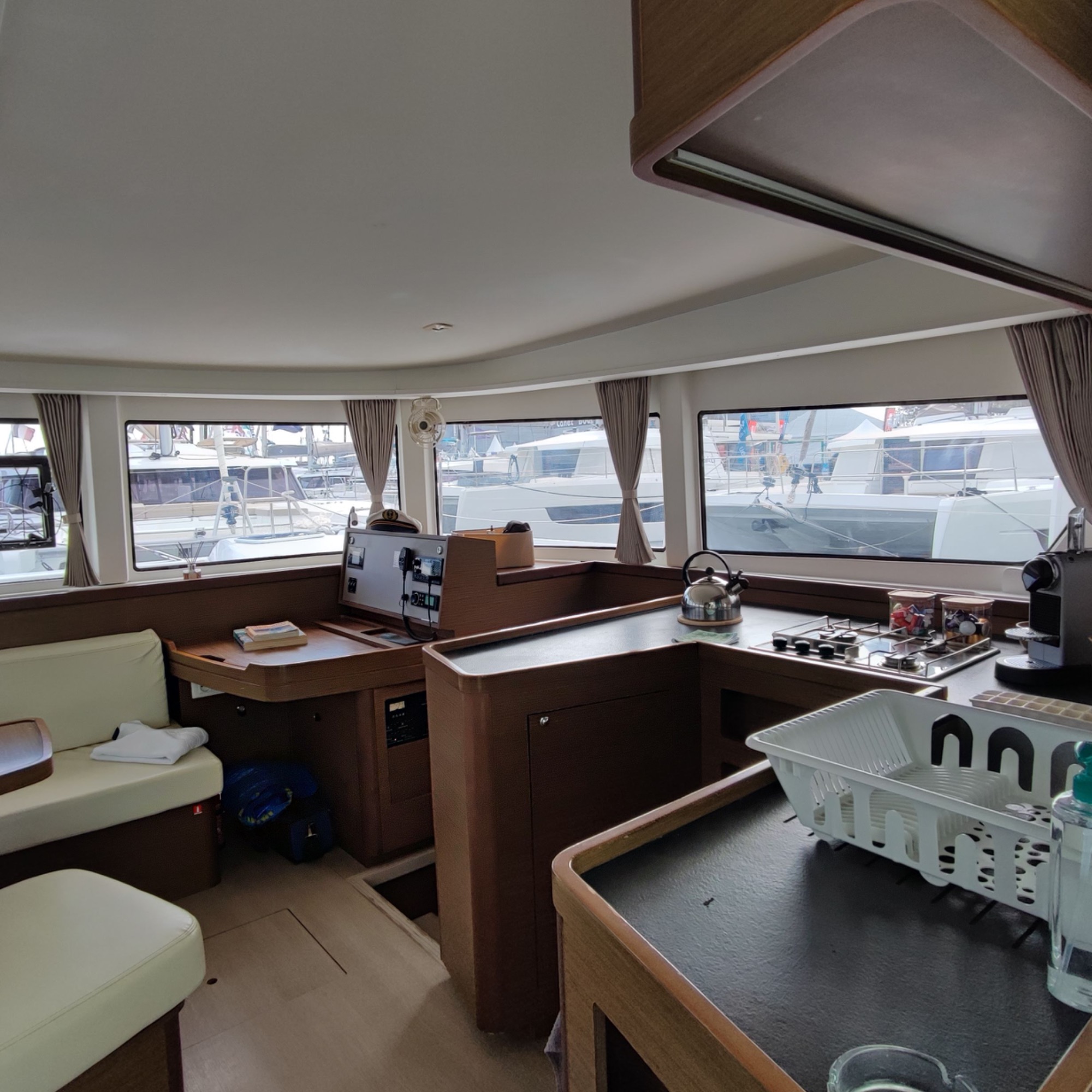 Lagoon 42 2021 Carré Intérieur d'un bateau avec des meubles en bois, bureau et fenêtres offrant une vue sur le port.