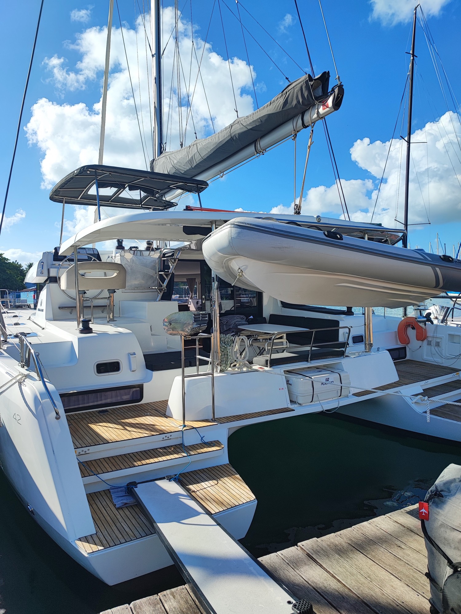 Lagoon 42 2021 Vue arrière Catamaran blanc amarré au port sous un ciel bleu avec des nuages.