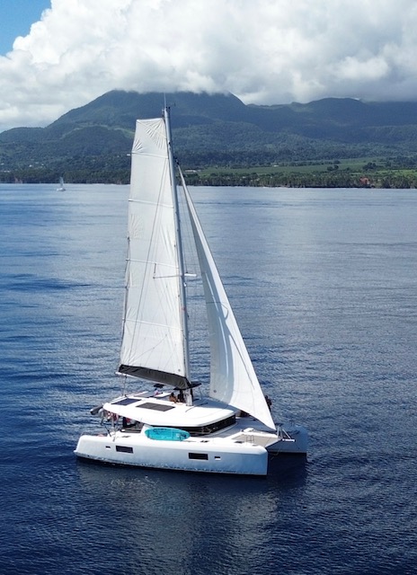Lagoon 42 2021 Sous voiles Catamaran naviguant calmement sur des eaux cristallines, entouré de montagnes verdoyantes.