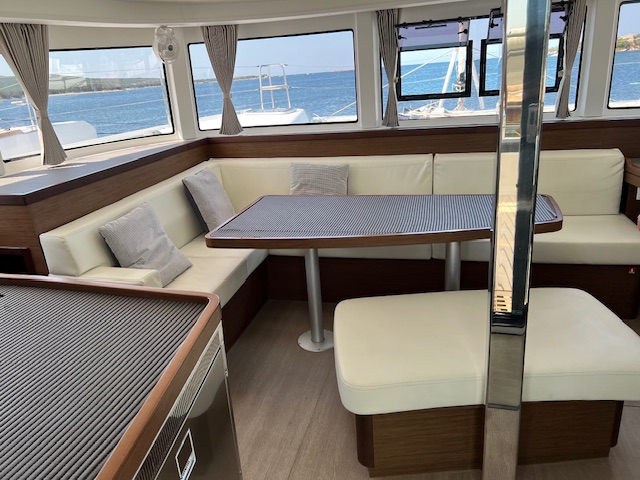 Lagoon 42 2021 Carré Intérieur d'un catamaran, espace salon avec canapé et table, vue sur la mer.