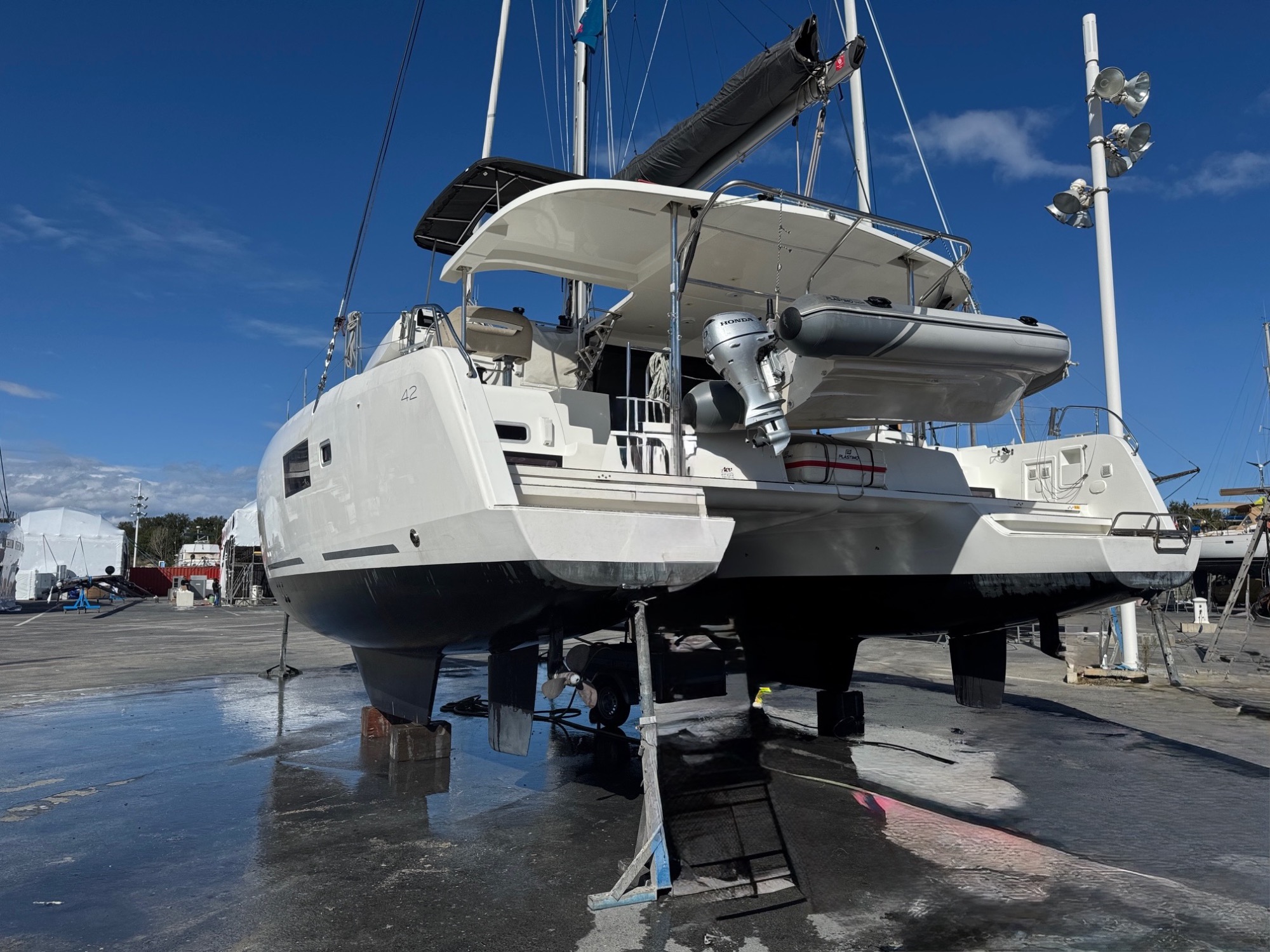 Lagoon 42 2021 A sec Catamaran sur support, à quai, avec un ciel bleu et des nuages en arrière-plan.