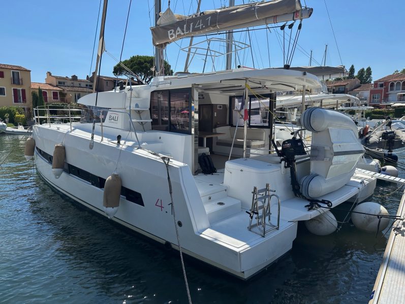 Grand Sud 55 Voilier blanc accosté dans un port, avec d'autres bateaux en arrière-plan. Ciel nuageux.