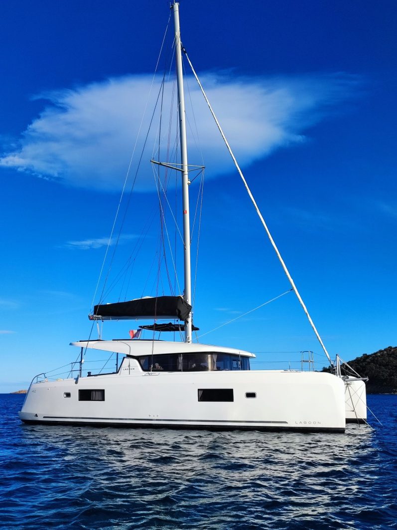 Grand Sud 55 Voilier blanc accosté dans un port, avec d'autres bateaux en arrière-plan. Ciel nuageux.